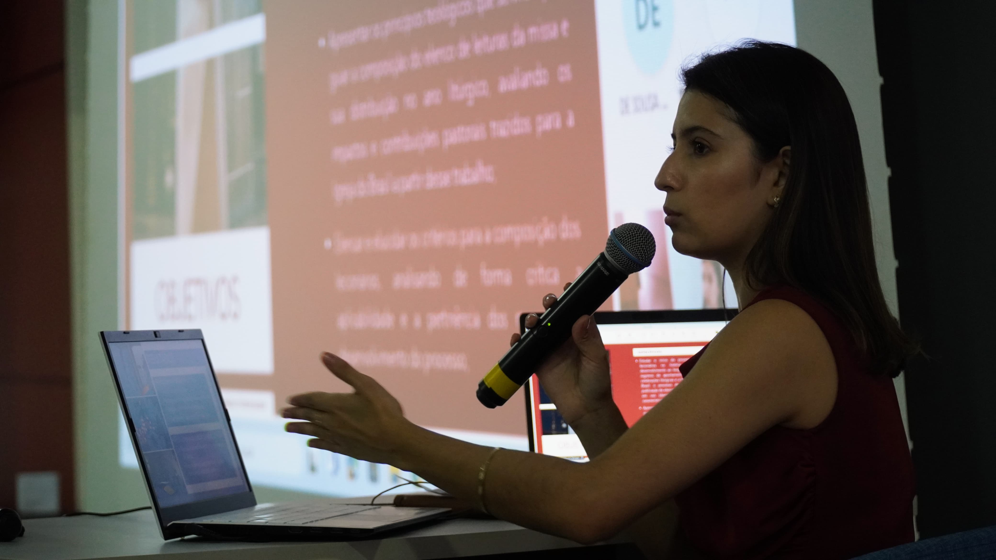 mulher falando ao microfone e apresentando trabalho