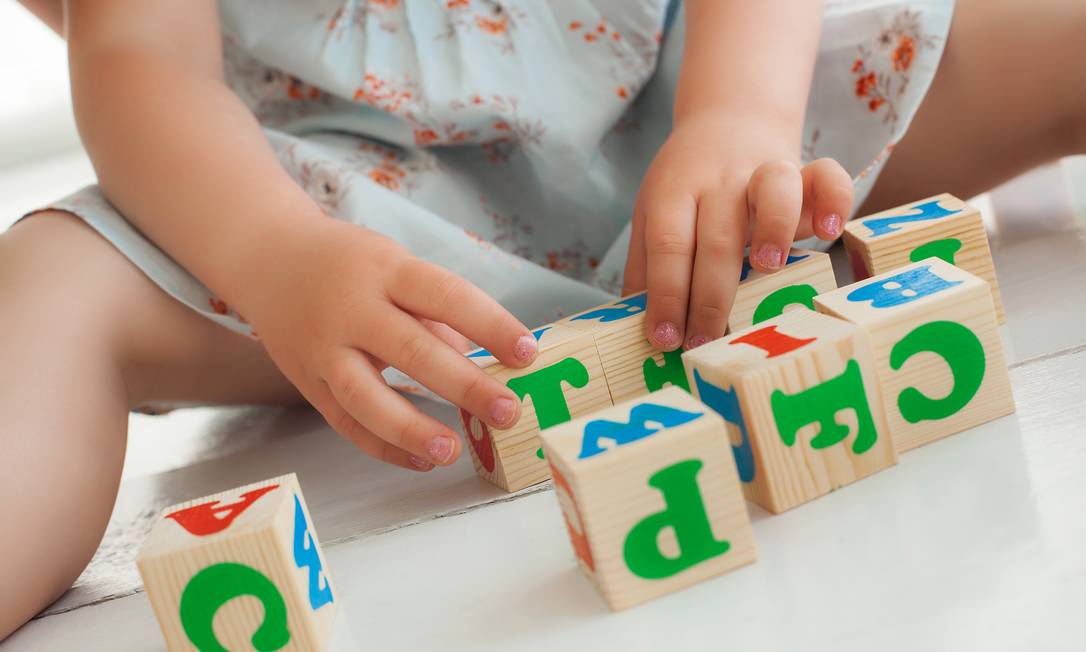 Criança brincando com letras em cubo de madeira sem aparecer o rosto