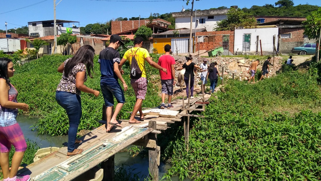 Alunos da universidade passando sobre ponte de madeira em comunidade