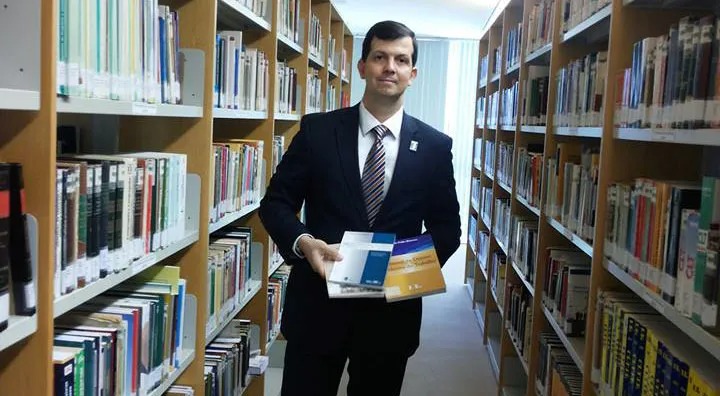 Fábio segurando livros na biblioteca